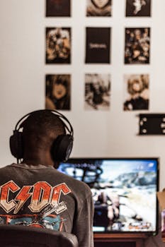 Person wearing headphones playing video game on computer screen at home.